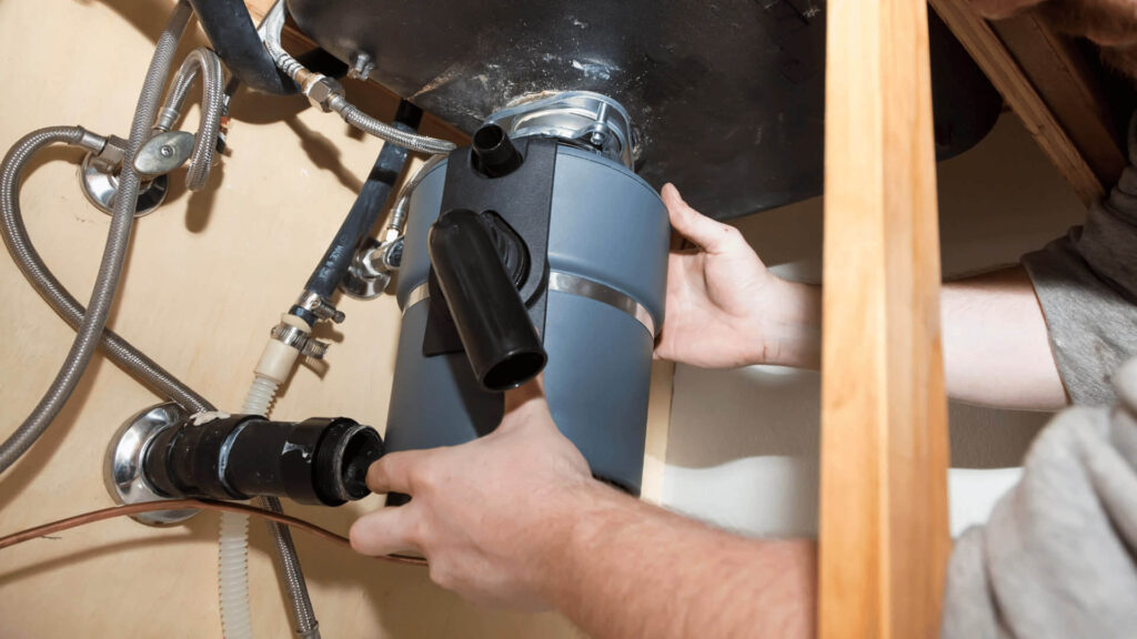 A plumber replacing a garbage disposal unit under the sink.