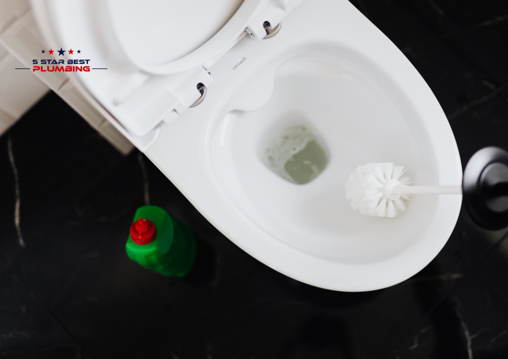 An overhead view of a white ceramic toilet being cleaned with a white scrub brush.