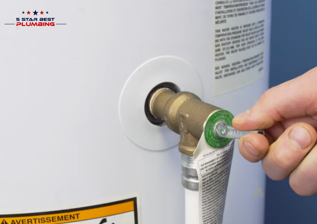 A close-up of a person's hand lifting the test lever on a brass Temperature and Pressure (T&P) relief valve on a white residential water heater.