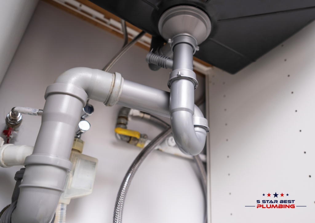 An under-sink view of gray plastic P-trap plumbing and drainage pipes connected to a kitchen sink.