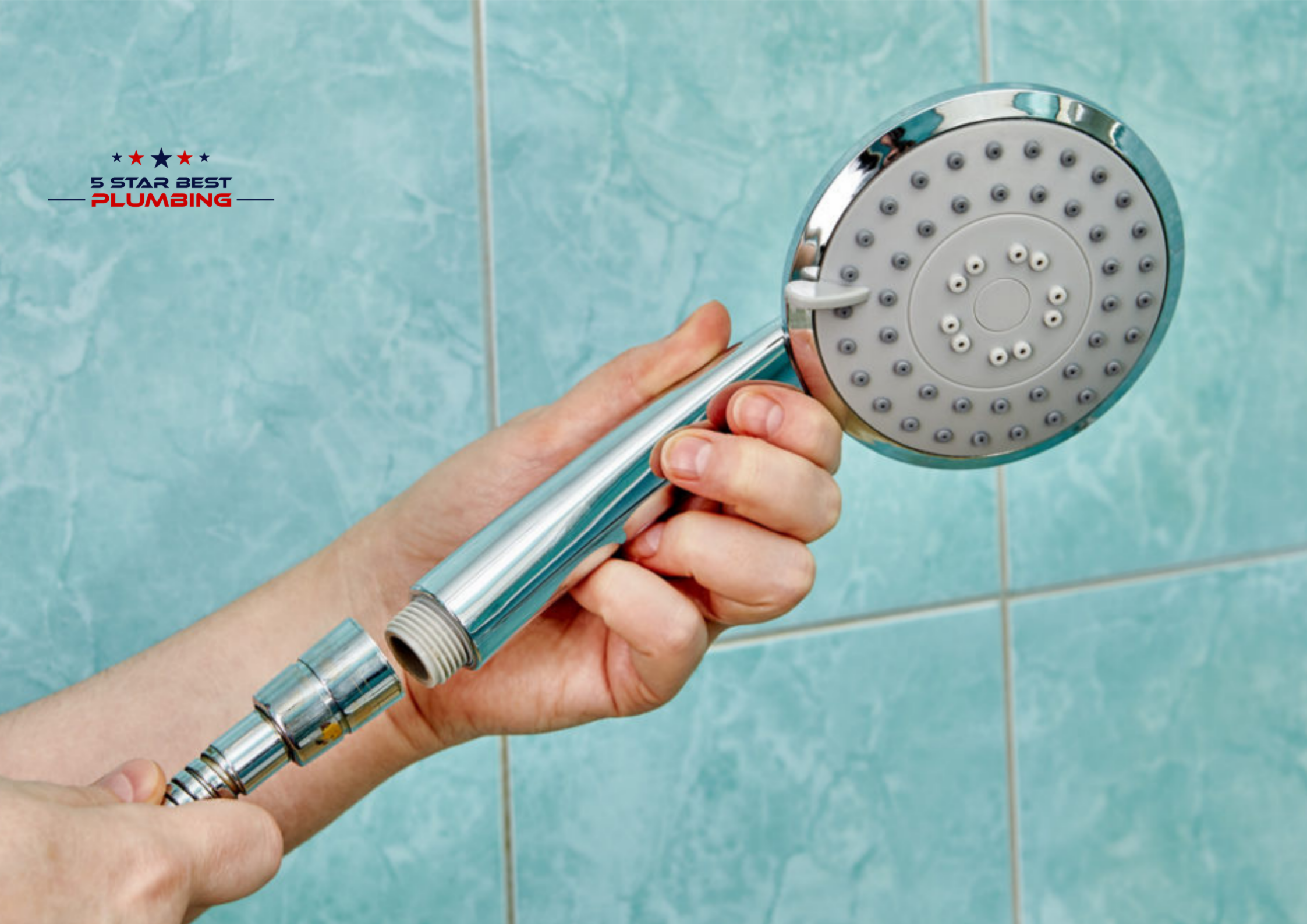 A close-up of a person unscrewing a chrome handheld shower head from its flexible hose, held against a background of light blue bathroom wall tiles.